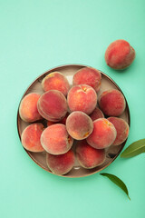 Sweet peaches and leaves on dark plate on mint background. Space for text