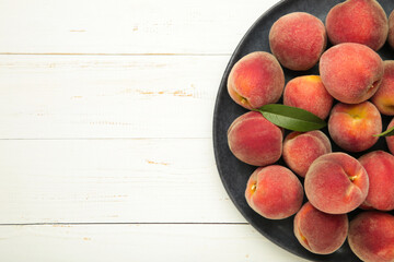 Sweet peaches and leaves on dark plate on white wooden background. Space for text