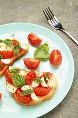Italian Caprese salad with cherry tomatoes, mozzarella, basil on mint plate on grey background.