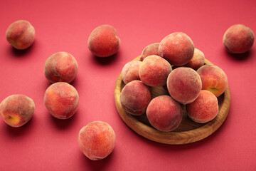 Sweet peaches and leaves on wooden plate on red background. Space for text