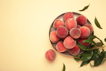 Sweet peaches and leaves on dark plate on beige background. Space for text