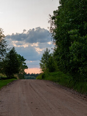 A peaceful rural road stretches into the distance under dramatic evening skies. The setting sun...