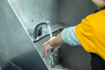 A child washes hands at a sink in a kitchen setting. 