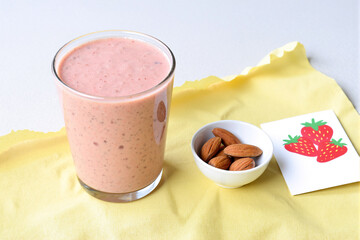 healthy and refreshing pink strawberry smoothie served in a glass with a side of almonds, set on a bright yellow napkin for a nutritious breakfast, snack, or light meal