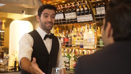 Focusing on smiling smart bartender preparing drinks at luxurious bar while engaging lively...