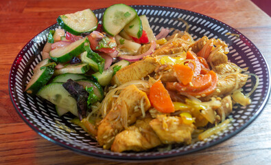 A dish with rice noodles and vegetable salad in a deep bowl on a wooden table