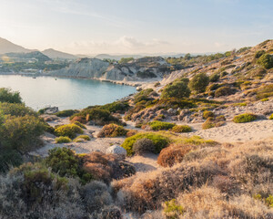 Obraz premium Earth and light in quiet rhythm — sun-kissed coastal hills and textured vegetation unfold toward a serene bay, inviting mindful exploration in Mediterranean stillness. Greece, Rhodes island