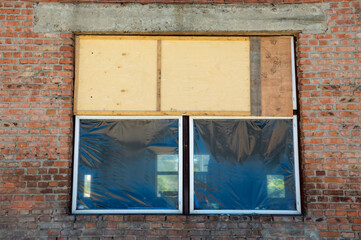 Boarded up windows with plastic sheeting reveal exposed brick at a construction site during...