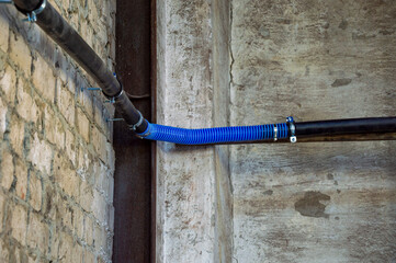 Blue flexible tubing connects metal pipes against a textured concrete wall in a contemporary...