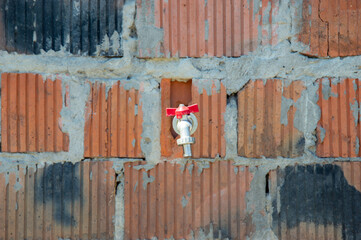 A water valve is mounted on a brick wall, showcasing signs of weathering and age while being part...