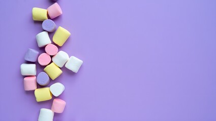 An arrangement of colorful marshmallow candies on a purple backdrop. The marshmallows are in various pastel shades, creating a playful and inviting composition.