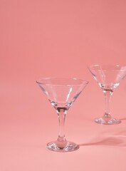 Two empty triangular martini or cocktail glasses on a pink plain background.