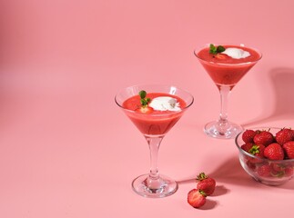 Non-alcoholic strawberry cocktail with ice cream scoop in triangle martini glasses on plain pink background. Valentine's day concept.