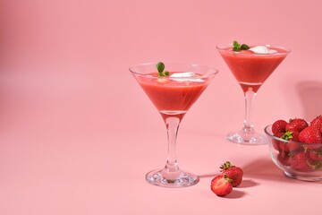 Non-alcoholic strawberry cocktail with ice cream scoop in triangle martini glasses on plain pink background. Valentine's day concept.