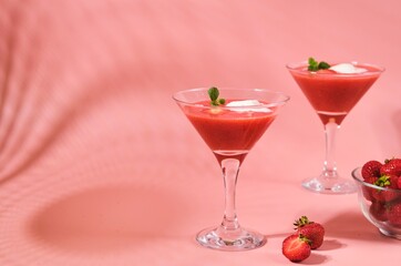 Non-alcoholic strawberry cocktail with ice cream scoop in triangle martini glasses on plain pink background. Valentine's day concept.