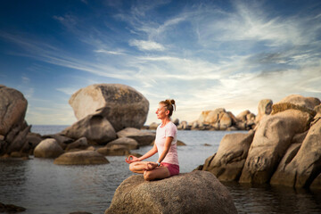 woman meditating on rock on the beach