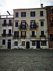 Historic buildings with balconies adorned with plants in a quiet Venetian square under a clear sky