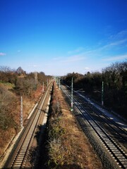 Train tracks stretch across a rural landscape under a clear blue sky in early afternoon