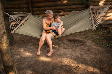 Emotional Mother and son are fooling around in hammock in summer forest. Family outdoor recreation,...