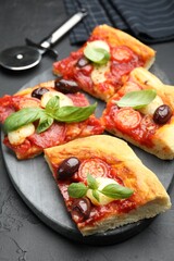 Pieces of tasty homemade pizza and cutter on black table, closeup