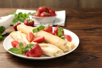 Tasty crepes with cream, strawberries and mint on wooden table, closeup