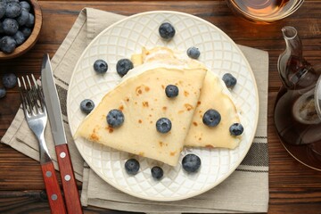 Tasty crepes with cream, blueberries and tea served on wooden table, flat lay