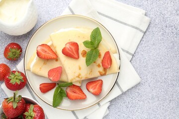Tasty crepes with cream, strawberries and mint on light gray textured table, flat lay