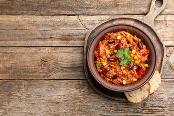 Tasty chili con carne in bowl and bread slices on wooden table, top view. Space for text