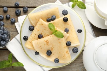 Tasty crepes with blueberries and mint on wooden table, flat lay