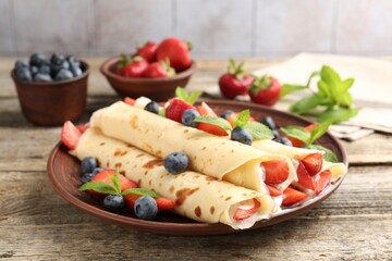 Tasty crepes with berries, cream and mint on wooden table, closeup