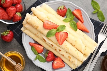Tasty crepes with strawberries and mint on grey table, flat lay