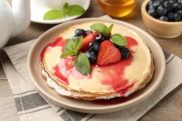 Delicious crepes with berries, sauce, cream and mint on wooden table, closeup