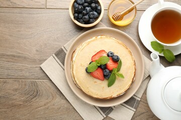 Delicious crepes with berries, cream, mint, honey and tea on wooden table, flat lay. Space for text