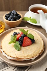 Delicious crepes with berries, cream, mint, honey and tea on table, closeup