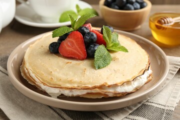 Delicious crepes with berries, cream, mint and honey on table, closeup
