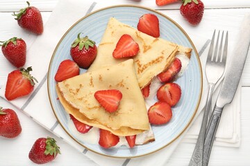 Delicious crepes with strawberries and cream on white wooden table, flat lay