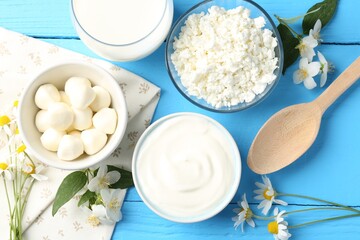 Different fresh dairy products and flowers on light blue wooden table, flat lay