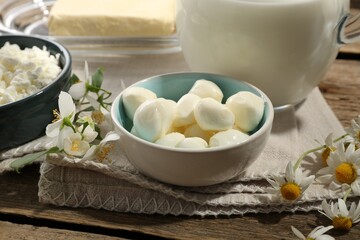 Different fresh dairy products and flowers on wooden table, closeup