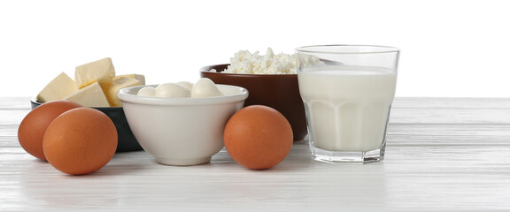 Different dairy products and eggs on wooden table against white background