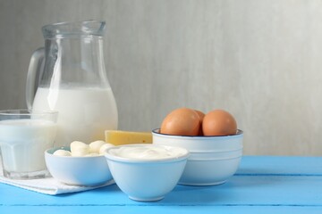 Different dairy products and eggs on light blue wooden table, space for text