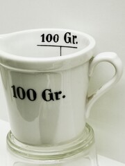 Ceramic measuring cup indicating 100 grams displayed on a glass surface for cooking demonstration...