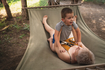 Emotional Mother and son are fooling around in hammock in summer forest. Family outdoor recreation,...