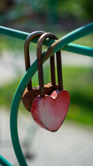 Padlock in shape of red heart hangs on fence. Symbol of eternal love and strong relationships. Vertical image