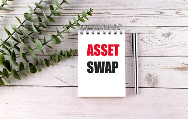 Notepad with text asset swap on white wooden table with green plant and silver pen