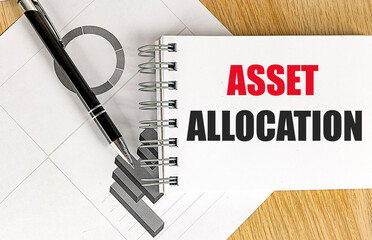 Notebook with text asset allocation on desk with financial charts and black pen
