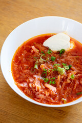 Traditional homemade borscht with sour cream and beef in white bowl