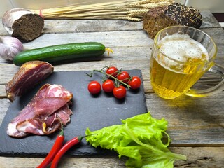 fragrant piece of dried meat on a cutting board next to vegetables and a glass of beer