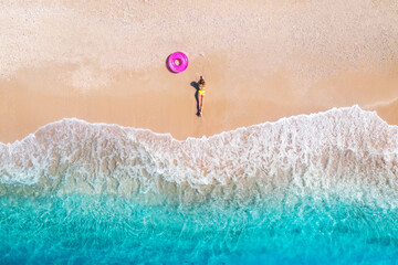 Aerial view of the lying beautiful young woman with pink swim ring on the sandy beach near sea with...