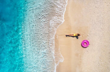 Aerial view with a woman sunbathing on a pristine white sand beach, surrounded by the turquoise...