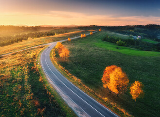 Aerial view of road, hills, green meadows and colorful trees at sunset in autumn. Top view of...